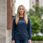 Woman wearing a navy blue sweatshirt and jeans standing outdoors with buildings in the background