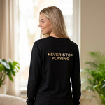 Woman wearing a black sweatshirt with 'Never Stop Playing' text in a living room.