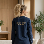 Woman wearing a navy sweatshirt with 'Never Stop Playing' text, standing in a modern living room.