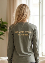 Person wearing a green sweatshirt with 'Never Stop Playing' text in a living room.